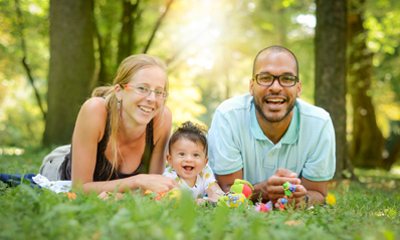 Woman, man and baby lying on grass in front of trees