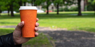 Person holding takeaway coffee cup in a park.