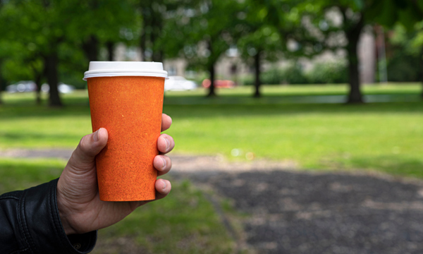 Person holding takeaway coffee cup in a park.