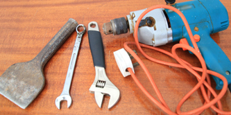 Tools, including a spanner and a powered drill, on a table.