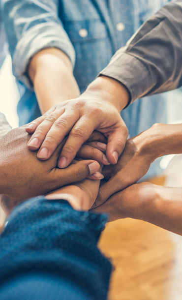 A group of eight people in a circle each holding out one arm with their hands stacked on top of one another's in the middle of the circle.