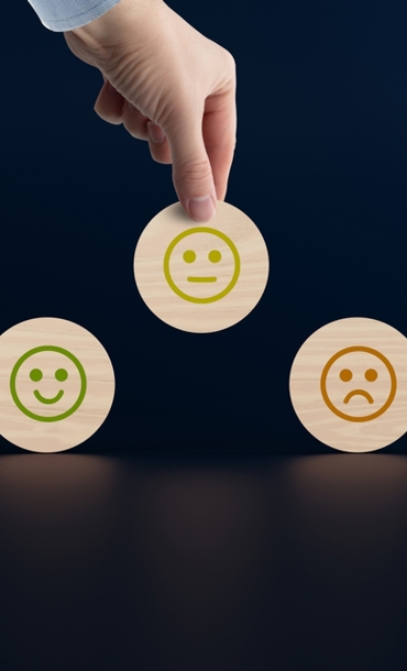 Wooden discs with icons of faces from happy to sad, a hand picks up a disc with an icon. The concept of evaluating, indicating the degree of satisfaction with the transaction.