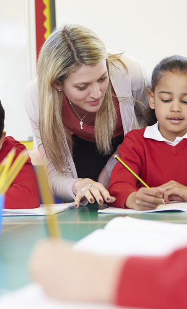 Teacher helping pupils reading and writing.