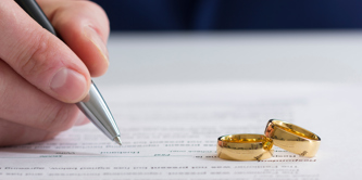 Person signing on paper with two wedding rings