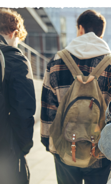 Young people walking along the street with a young girl looking behind.