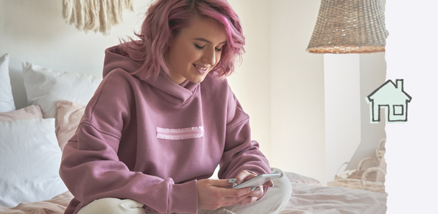 nojs A young woman sat on a bed while looking at her mobile phone.