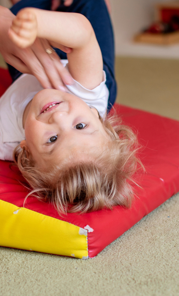 Child on a foam mat supported by adult hands